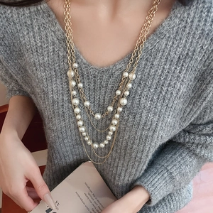 Macro detail of multilayered faux pearl necklace with gold chain on grey sweater