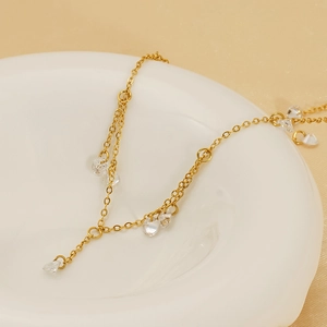 Minimalist gold chain necklace with sparkling water-drop crystal pendants on a ceramic plate