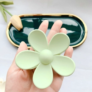 Close-up of matte mint green flower hair claw clip held over a ceramic decorative plate