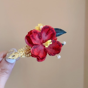 Detailed shot of red silk flower hair clip with pearls and golden leaf accents