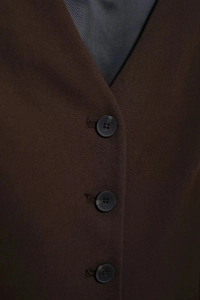 Détail de boutons en résine noire sur le tissu tissé marron foncé d'un gilet chic