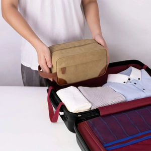 Vintage men's canvas toiletry bag being placed into a suitcase for travel storage.