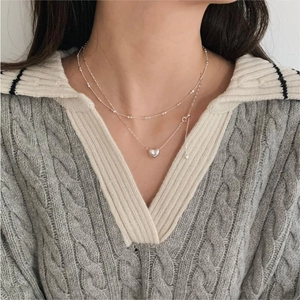 Detail of layered sterling silver necklaces with heart pendant on a gray knit sweater