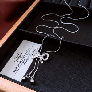 Macro detail of silver bow pendant with zircons and tassels on a snake chain