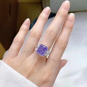 Detailed close-up of a purple radiant cut gemstone ring with side diamonds on model hand
