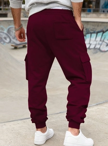 Rear view of burgundy stacked cargo sweatpants with elastic cuffs in an outdoor urban setting
