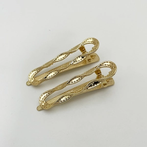 Detailed view of two gold metal hair clips with hollow wave texture design on white background