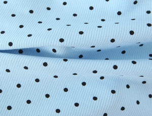Macro shot of light blue ribbed knit fabric with small black polka dots texture