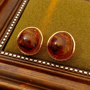 Macro detail of amber resin earrings with gold trim on an olive textured fabric