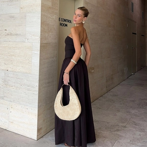 Elegantes schwarzes trägerloses Maxikleid mit voluminösem Rock und gewebter Strohhandtasche