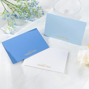Close-up of three gold-stamped Thank You greeting cards on elegant gauze with blue flowers