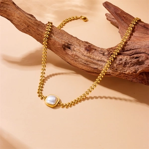 Golden wheat chain necklace with square pearl pendant draped on a wooden branch