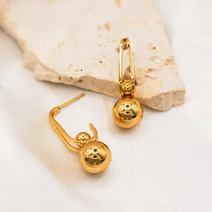 Macro detail of high-polish 18k gold-plated spherical drop earrings on silk background