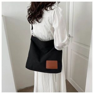 Detail of black canvas tote bag with brown leather patch and adjustable shoulder strap