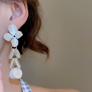 Close-up of white flower earrings with petal tassels and shimmering shell texture