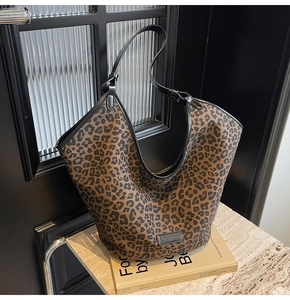 Detail of leopard print tote bag with black leather straps on a marble surface