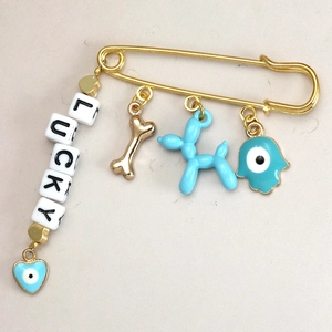 Detail of golden safety pin brooch with lucky letters and blue hamsa hand charm