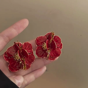 Close-up of red flower earrings with gold edges held by hand to show size and detail