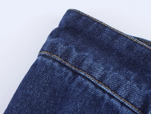 Détail de la taille du jean bleu foncé avec coutures jaunes contrastées et texture du denim