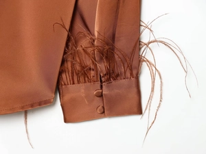 Detailed close-up of caramel satin shirt cuffs with luxury feather trim and fabric buttons