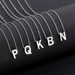 Detail of five silver stainless steel letter necklaces P Q K B N on a dark textured surface
