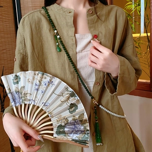 Détail du collier à pampilles en perles de cristal sur chemise en lin vert et éventail