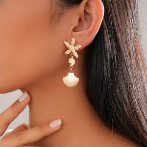Detail of gold seashell starfish drop earrings on model for beach style holiday look