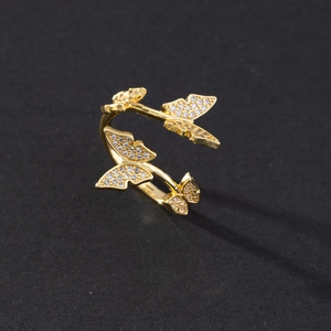 Adjustable golden butterfly ring with sparkling zircons on a textured black background