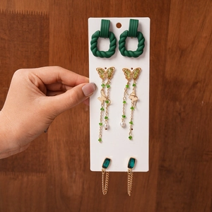 Three pairs of golden butterfly and green gemstone earrings displayed on a white card
