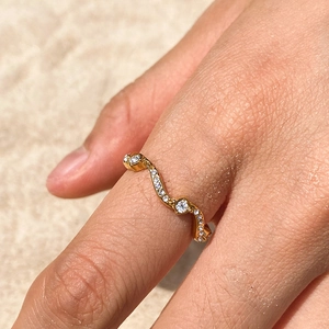 Gros plan d'une bague ondulée plaquée or avec strass portée au doigt sur la plage
