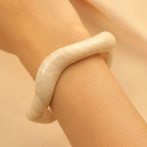 Detailed view of irregular cream wavy resin bangle with marbled texture on model's wrist