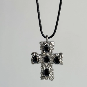 Close-up of a silver cross pendant with black stones on a black cord necklace