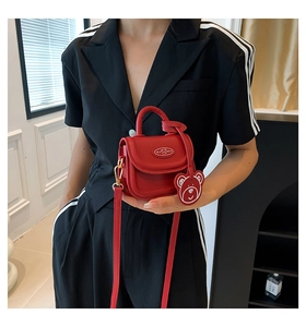 Mini red crossbody bag with cute bear charm shown on model in a black striped suit