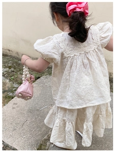 Rear view of girl in beige lace embroidery top and cake skirt with pink pearl handbag