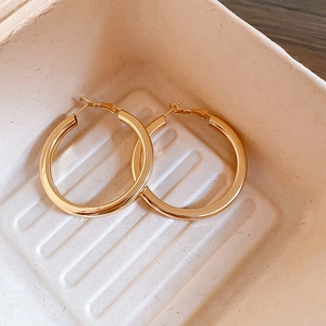 Detailed view of polished golden hoop earrings in a minimalist textured display tray