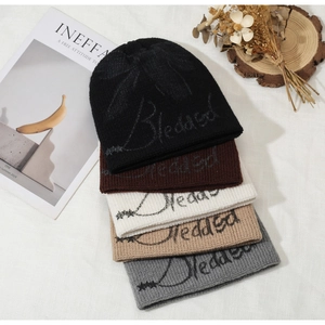 Detailed view of five stylish winter knit beanies in various colors with script embroidery.