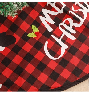 Close-up of red and black plaid Christmas tree skirt with Merry Christmas text and holly leaf