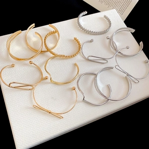 Detail shot of assorted gold and silver minimalist open metal bracelets on a white tray