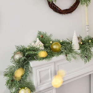 Artificial Christmas garland with warm lights, pine needles and ornaments on a white fireplace