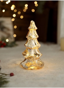 Close-up of golden LED Christmas tree ornament with warm bokeh lights and snowy base
