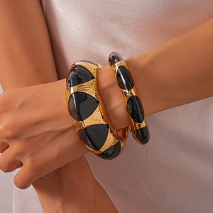 Close-up of set of two vintage hammered gold metal cuffs with black enamel drip detail