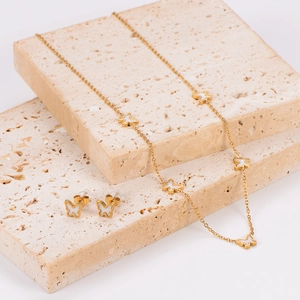Elegant gold butterfly necklace and earrings set with white shell inlay on stone stand
