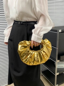 Detail of metallic gold pleated cloud bag with seamless handle on minimalist model outfit