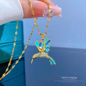 Macro detail of golden hummingbird pendant with blue enamel and sparkling zircons