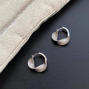 Silver twisted texture hoop earrings with minimalist metal design on textured fabric