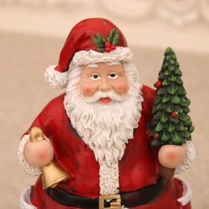 Detail of Santa Claus resin figurine holding a bell next to a decorated Christmas tree