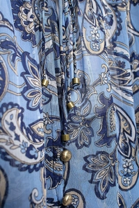 Dettaglio della camicetta in chiffon paisley blu con lacci e decorazioni in perline