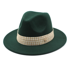 Detail of dark green wool fedora hat featuring tweed band and gold metal M logo