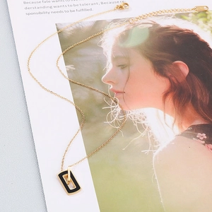 Détail du collier pendentif carré en or rose avec émail noir posé sur un magazine de mode