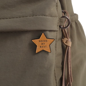 Macro shot of a yellow glitter star pin with 'DOING MY BEST' text on a green backpack
